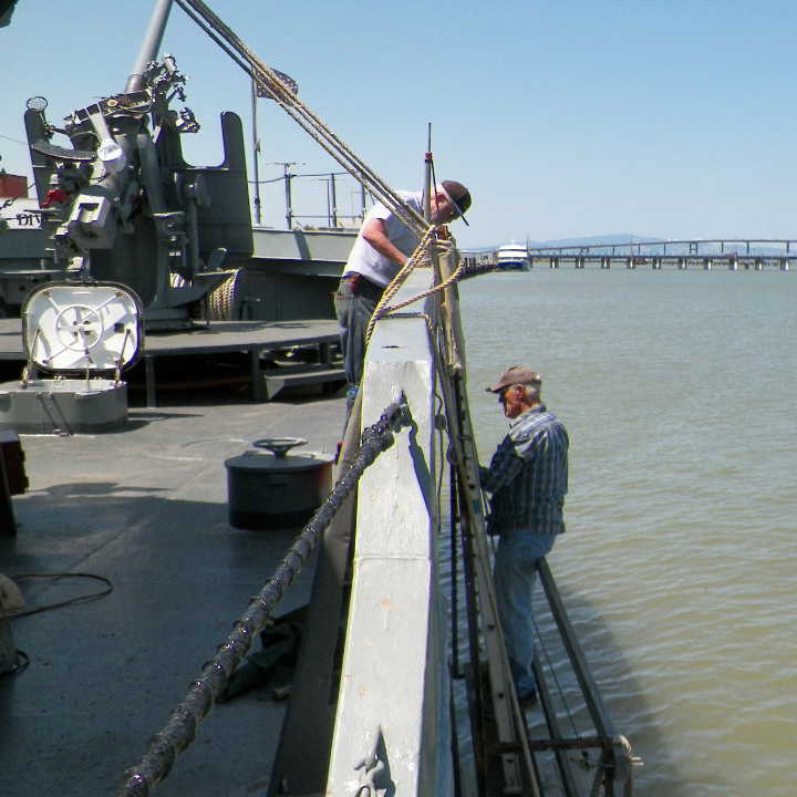Volunteer Crew Members Allan J. & Bill H. repaint the starboard side of the USS LCS-102 as part of restoration.